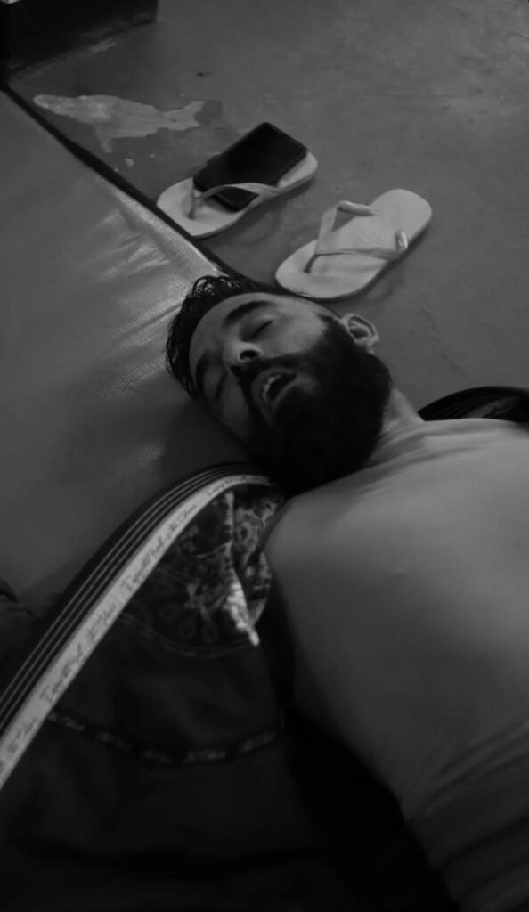 Homem branco com barba deitado estirado no tatame. Feições demonstram exaustão.